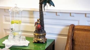 A room with a green side table holding a glass container with a drink, a decorative statue, and a wicker chair with a cushion.