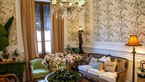 A room with a green armchair, a sofa with multiple cushions, a chandelier, and a table with a flower arrangement. - Villa Vicuña Hotel Boutique (Salta)