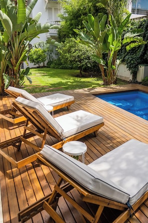 A wooden deck with lounge chairs and a small round table. - Villa Vicuña Hotel Boutique (Salta)