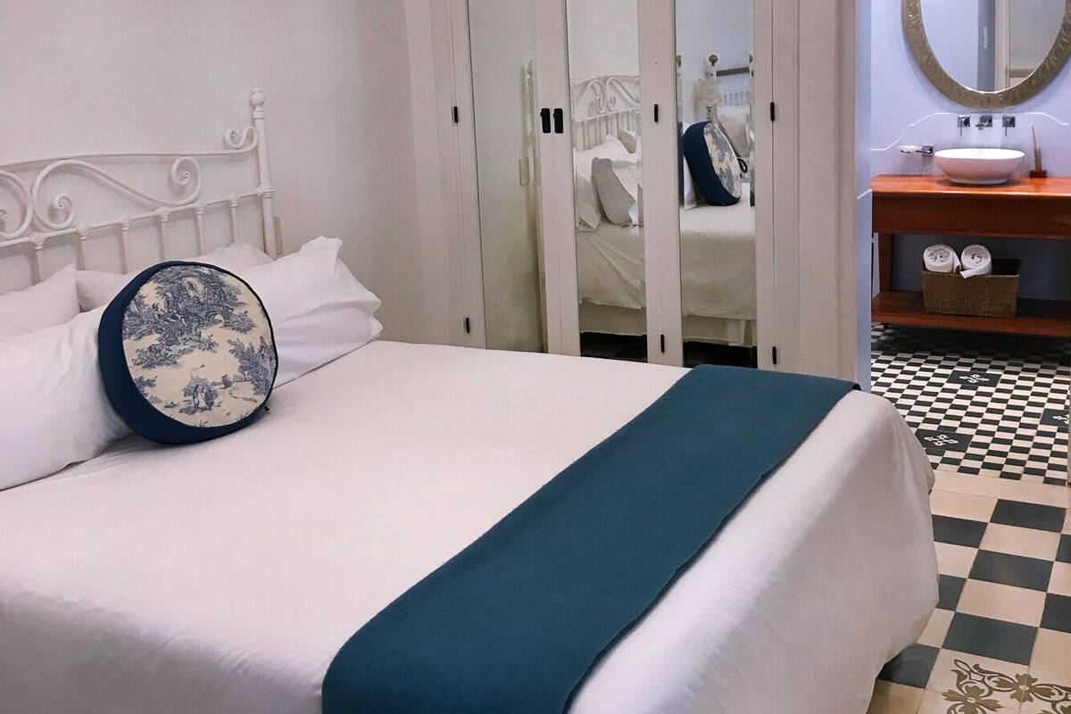 A neatly made bed with a blue throw blanket, white bedding, and a decorative pillow.