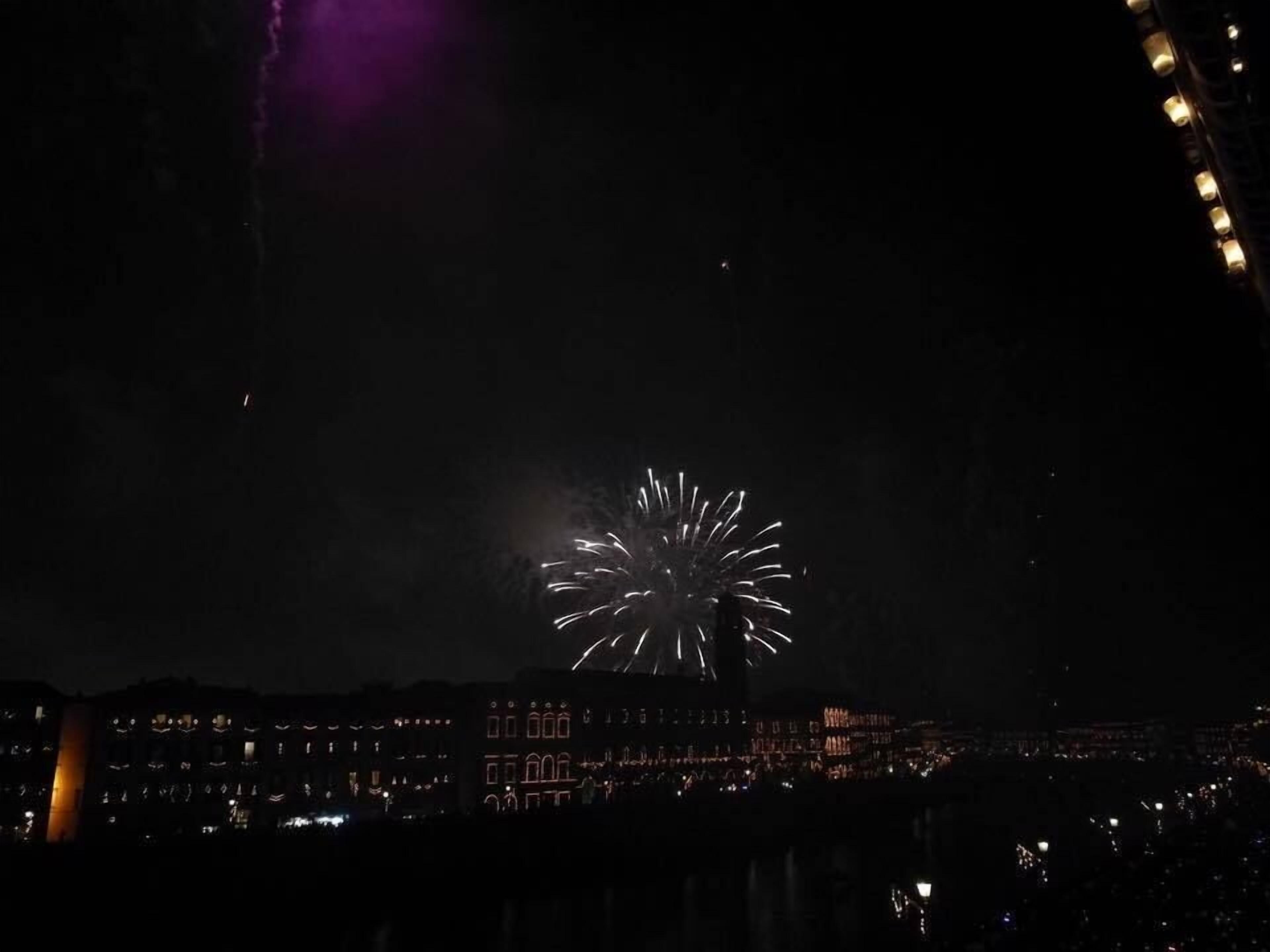 A nighttime view of a cityscape with buildings and a firework display.