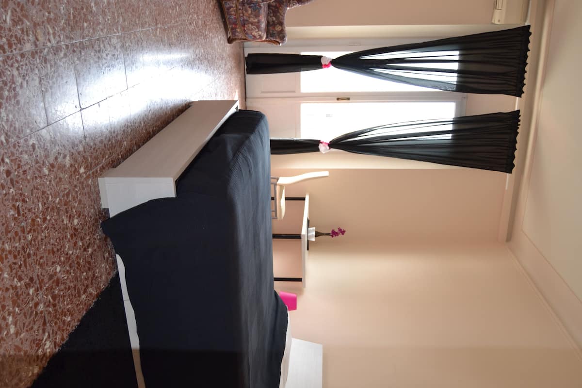 Una habitación con sofá, una mesita, una silla y una ventana con cortinas.