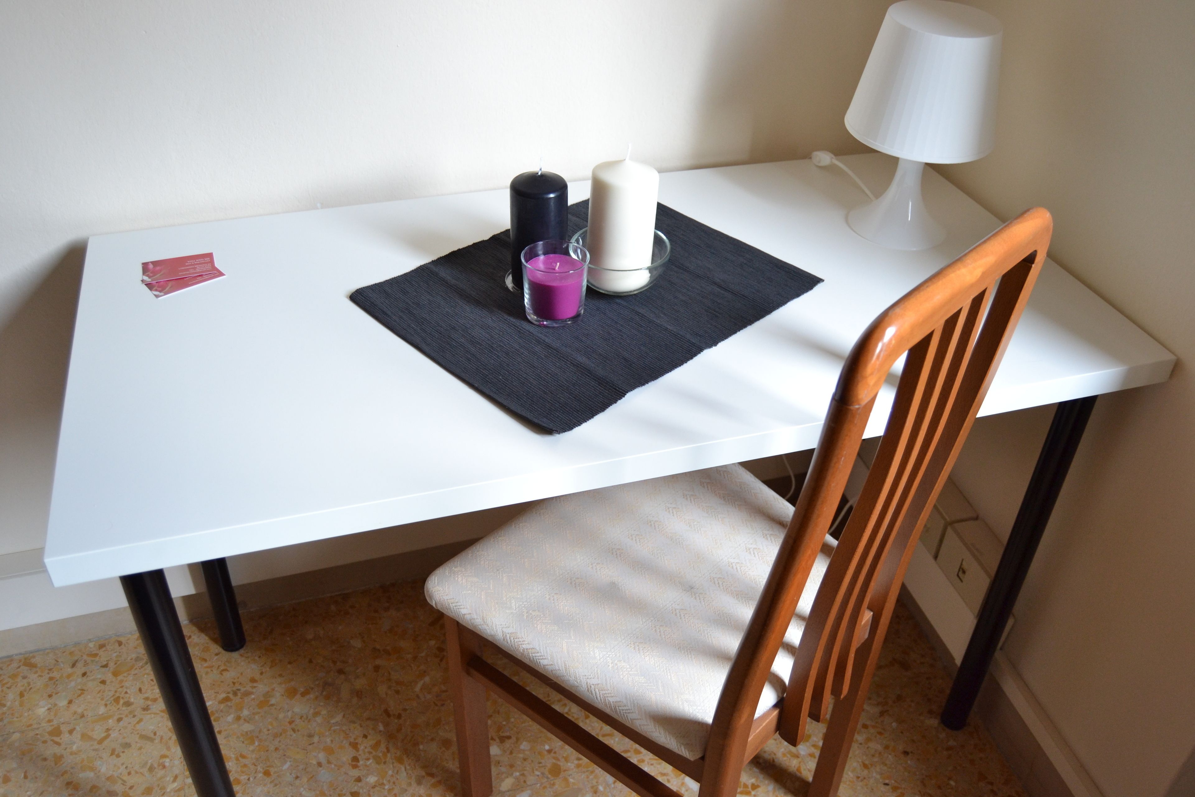 Ein weißer Tisch mit schwarzer Tischdecke, einer violetten Kerze, einer weißen Kerze und einer weißen Lampe.