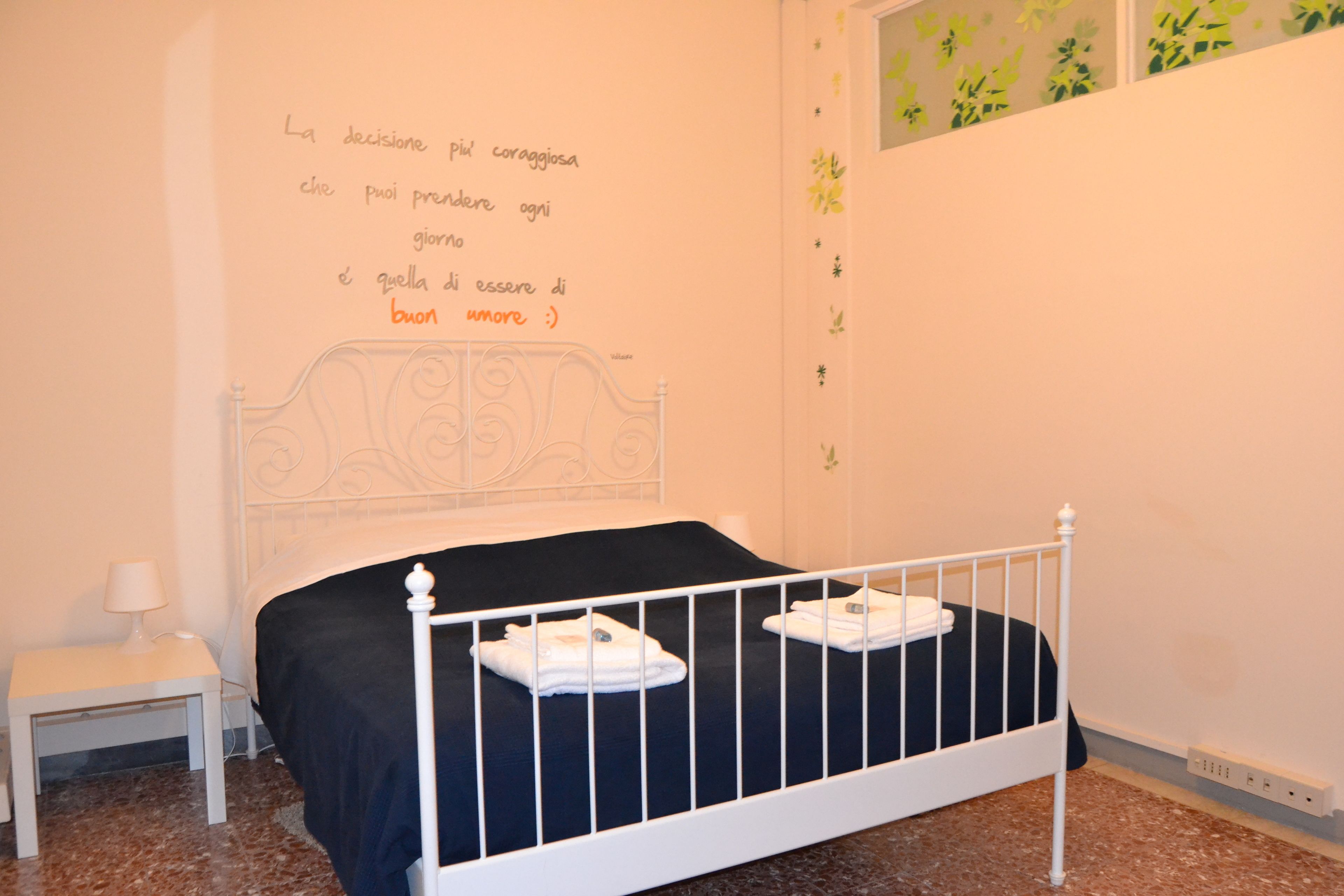 A bedroom with a white metal bed frame, a black bedspread, and a small bedside table with a lamp.