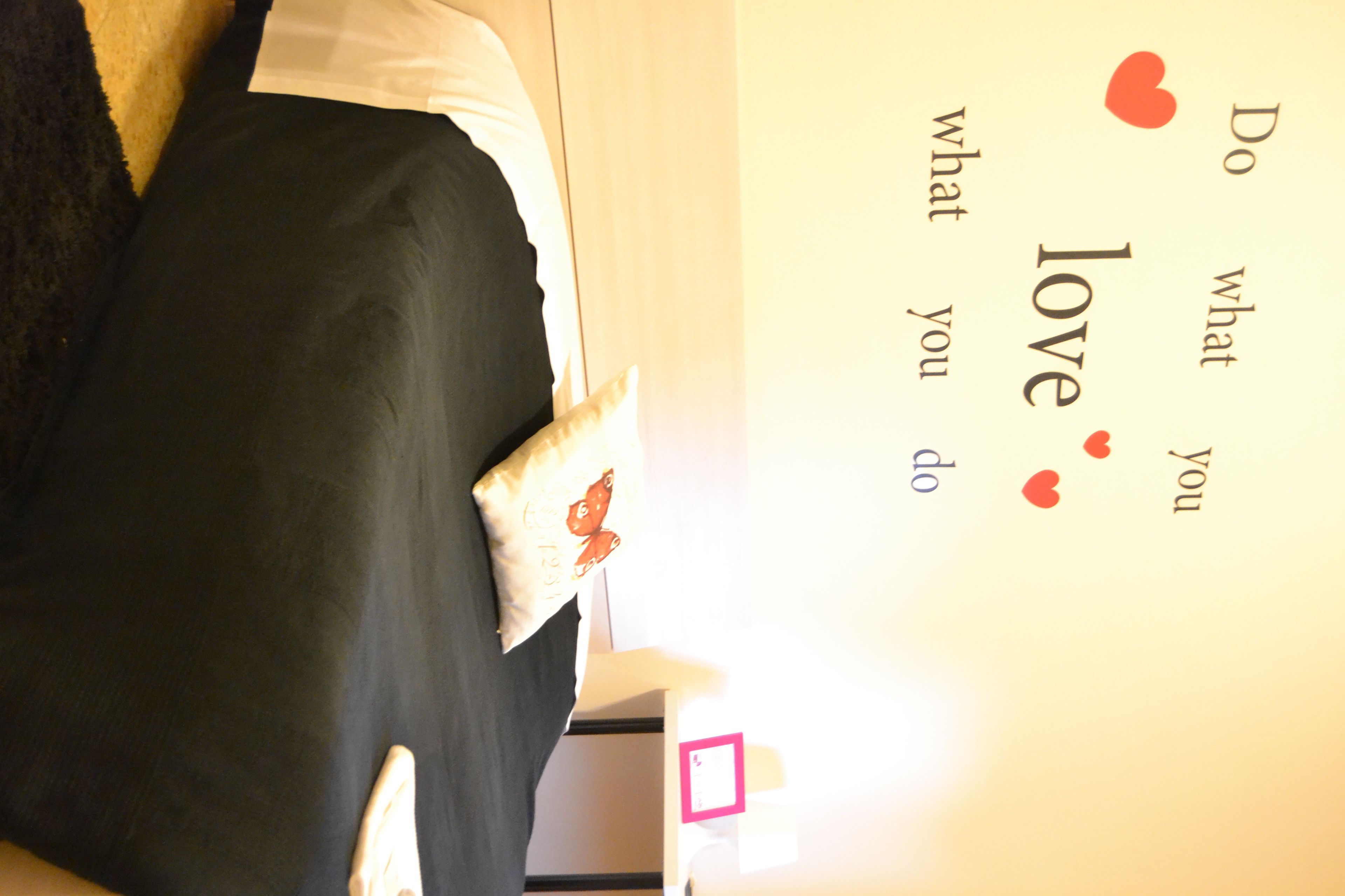 Una cama con un almohadón de diseño de mariposa, una pared con una frase motivacional y un pequeño cuadrado rosa en la pared.