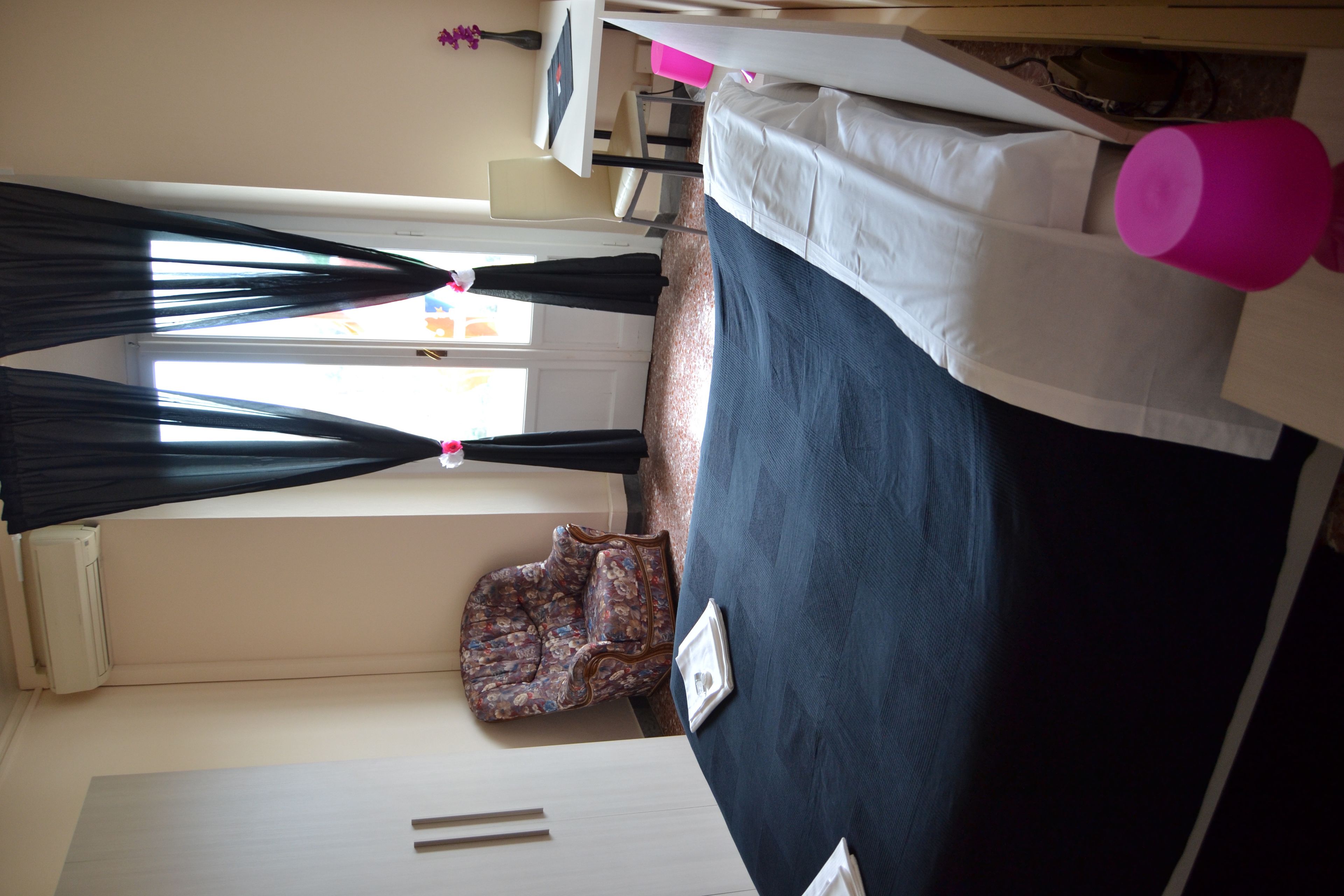 A room with a bed, a window with curtains, a chair, and a small table.