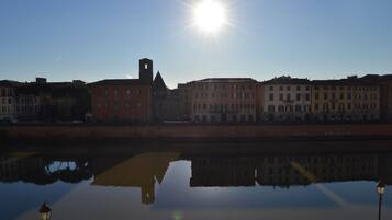 Un río tranquilo que refleja edificios, un cielo despejado y un sol brillante.