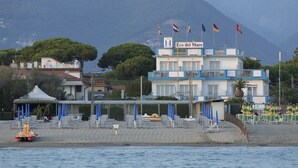 A hotel with a terrace, beach chairs, umbrellas, and flags. - Hotel Eco del Mare (Massa)