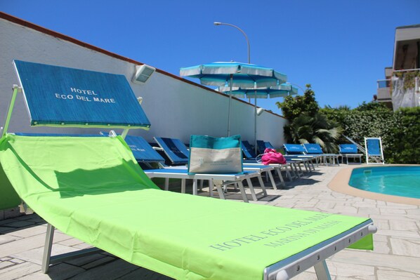 Zona de piscina con sillones y sombrillas en el Hotel Eco del Mare.