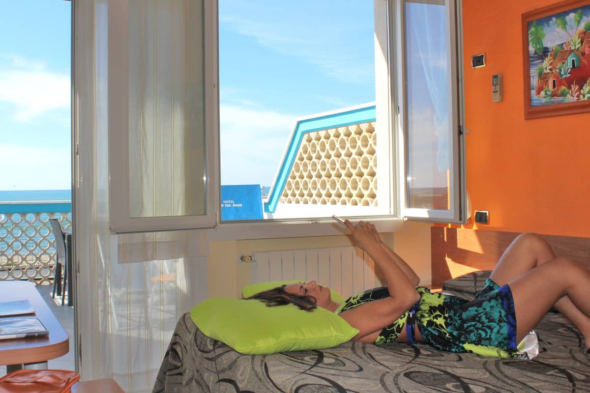 A room with a bed, a window, and a view of the sea.