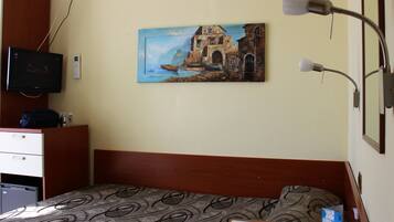 Habitación de hotel con cama, escritorio con computadora, un cuadro de paisaje costero y una lámpara.