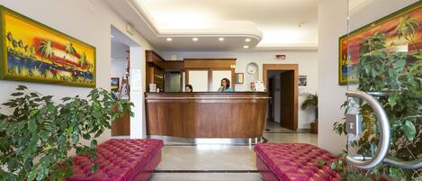 Un vestíbulo de hotel con un mostrador de recepción, dos sofás rosados y un cuadro grande en la pared.