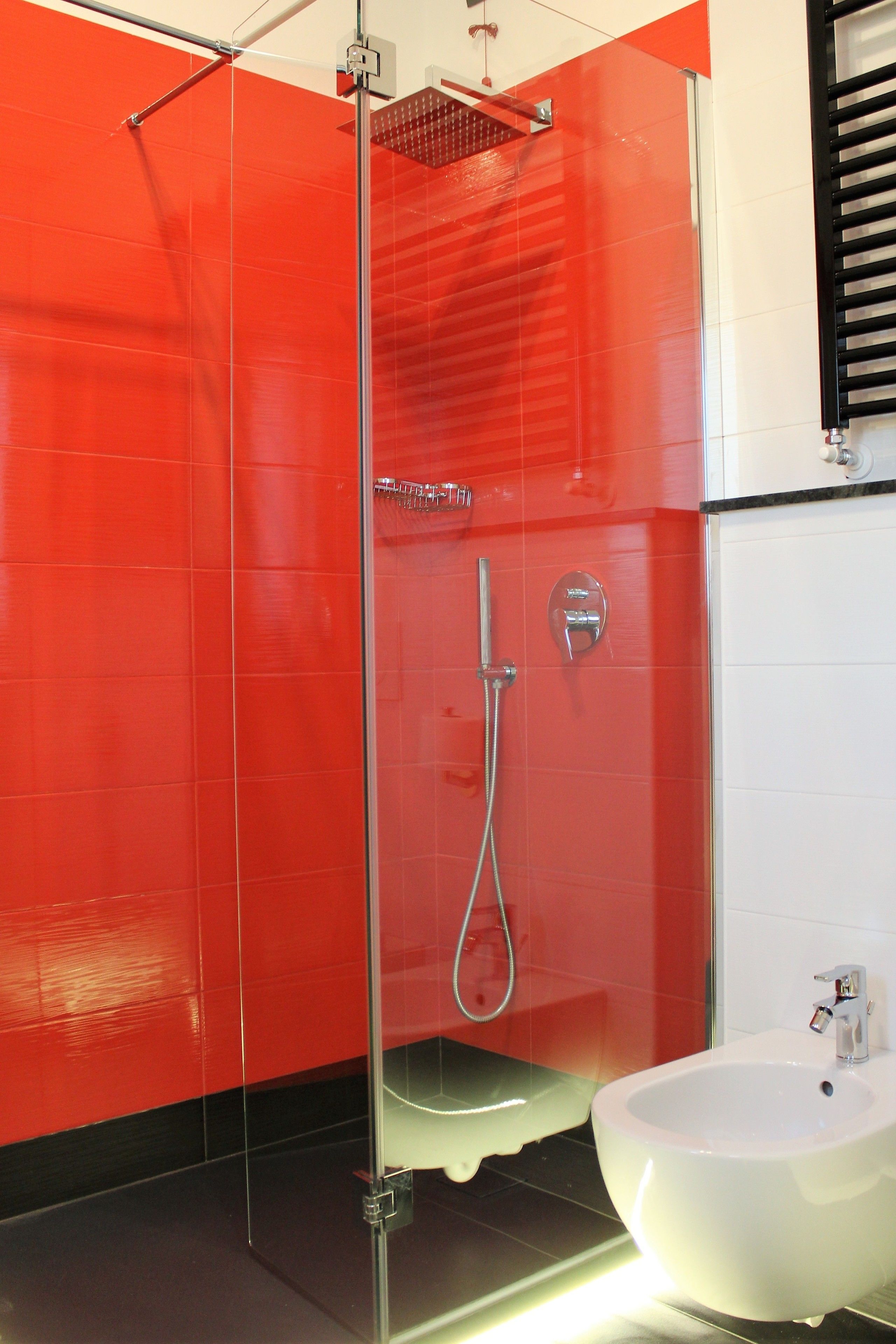 Ein modernes Badezimmer mit einer gläsernen Duschkabine, einem weißen Waschbecken und roten Fliesenwänden.