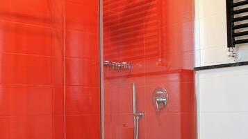 Ein modernes Badezimmer mit einer gläsernen Duschkabine, einem weißen Waschbecken und roten Fliesenwänden.