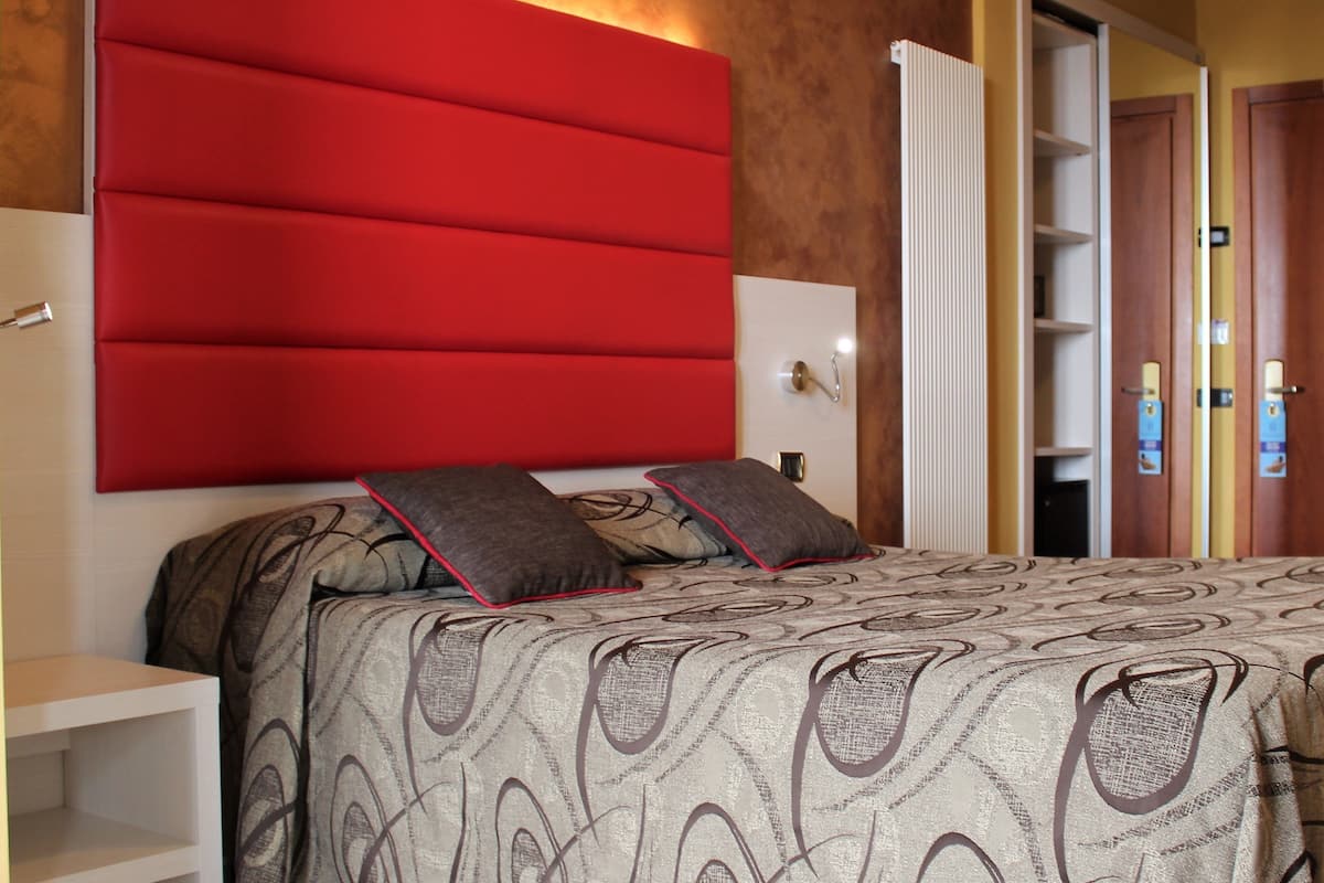 A bedroom with a large red headboard, patterned bedding, and a wardrobe with a mirror.
