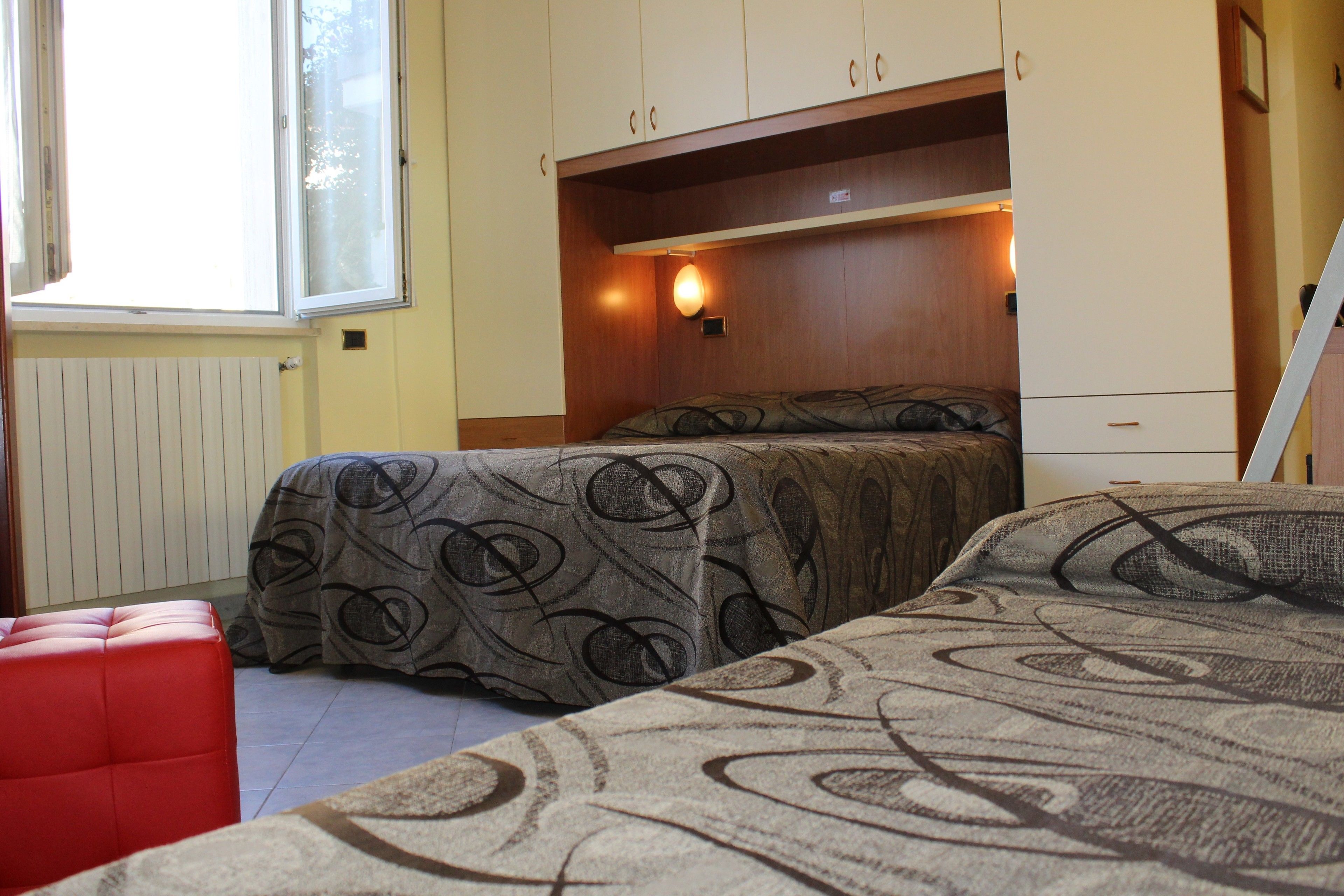 Un dormitorio con dos camas, un banco rojo y una ventana.