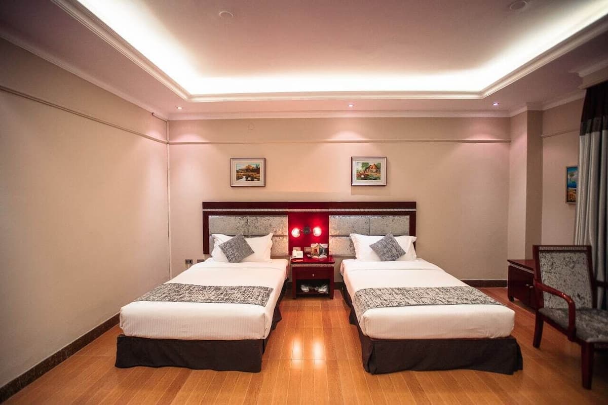 A hotel room with two beds, a nightstand with a lamp, and a chair.