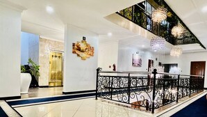 Een ruime lobby met een gepolijste vloer, een decoratieve balustrade en een trap naar een hoger niveau.