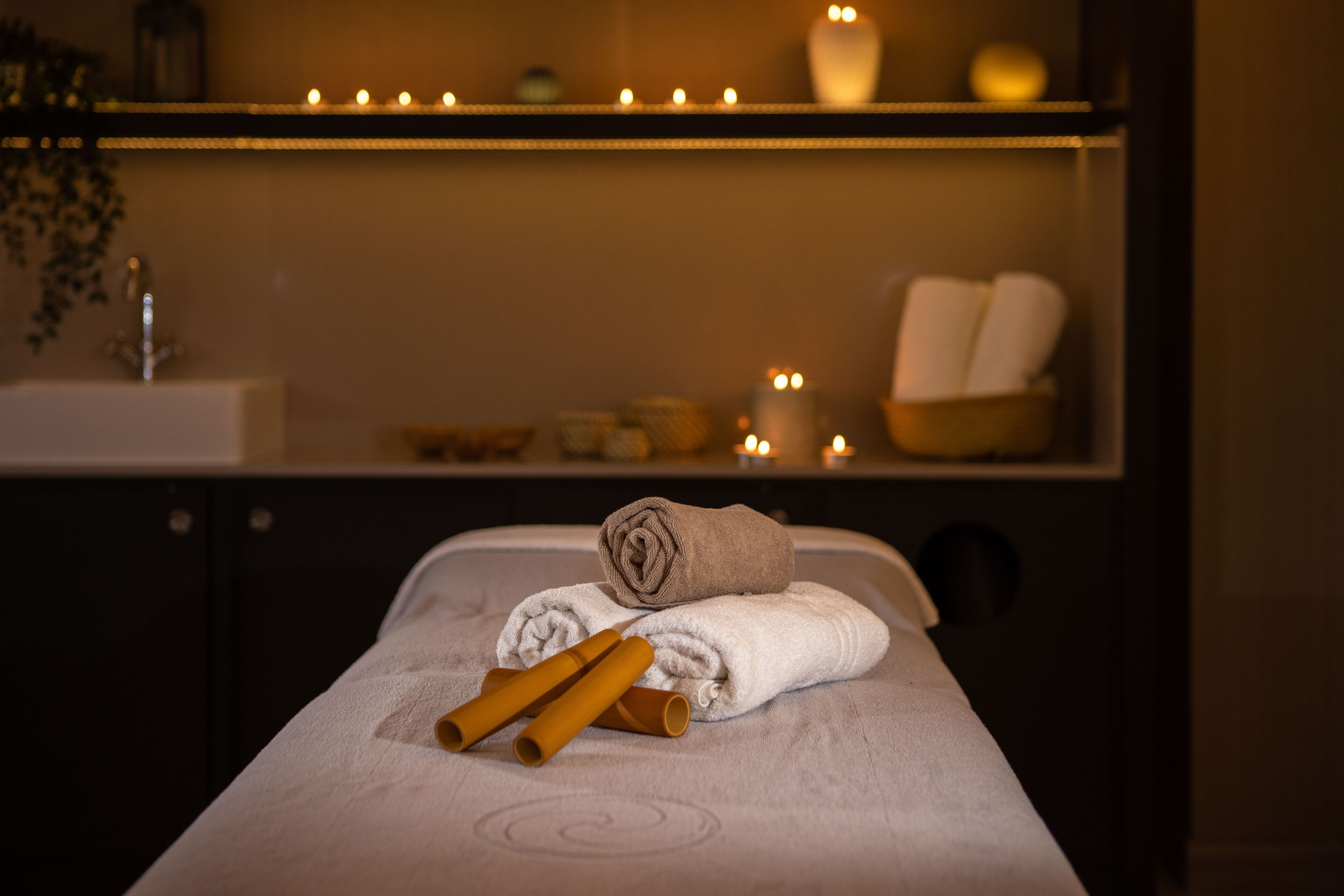 A massage table with towels and candles, a sink, and a shelf with candles and toiletries.