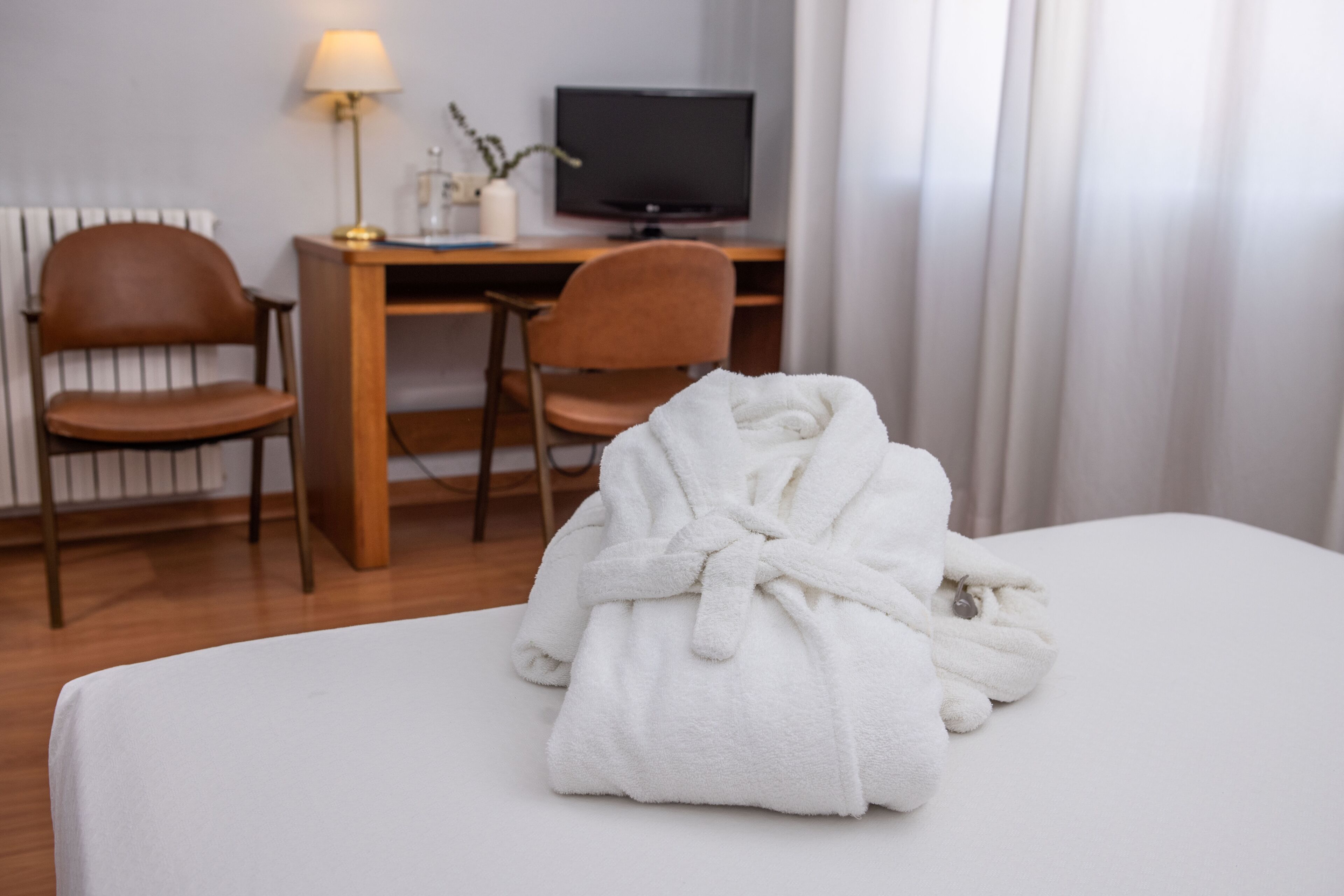 Una habitación de hotel con una cama, un escritorio con una computadora, dos sillas y una lámpara.