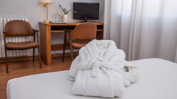 Una habitación de hotel con una cama, un escritorio con una computadora, dos sillas y una lámpara.