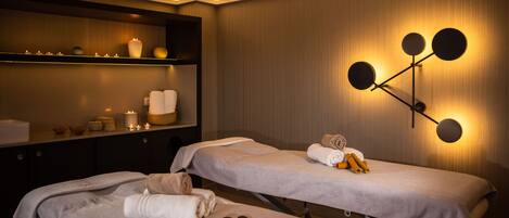A spa room with two massage tables, candles, and a wall-mounted light fixture.