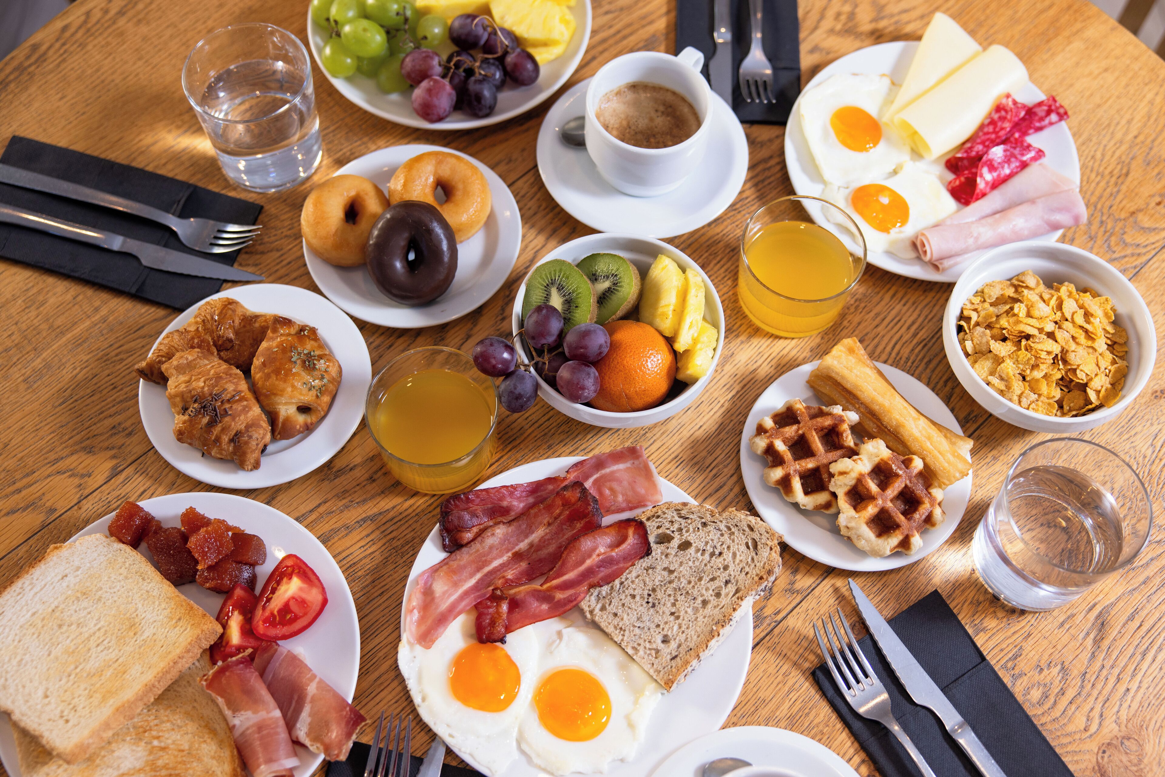 A breakfast table with plates of eggs, bacon, toast, and various fruits and beverages.
