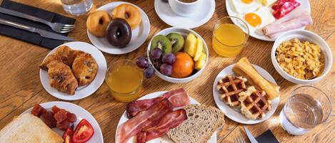 A breakfast table with plates of eggs, bacon, toast, and various fruits and beverages.
