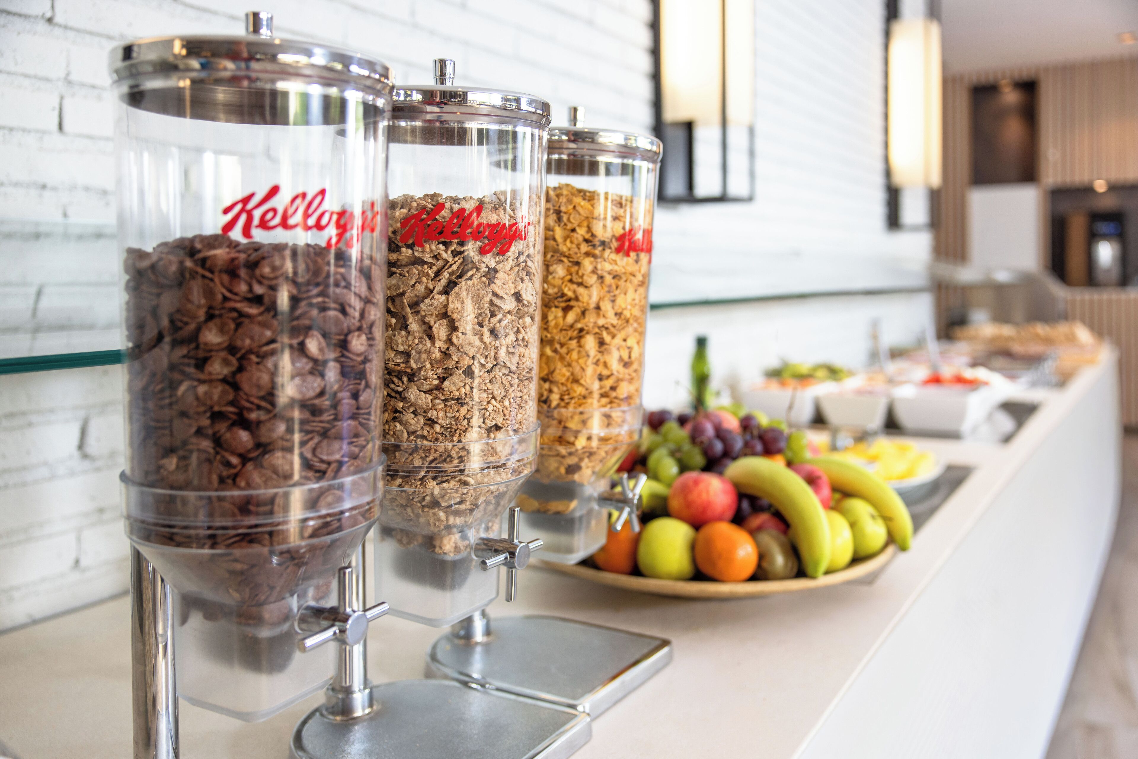 Tres dispensadores de vidrio transparente con etiquetas 'Kellogg's', que contienen granos de café y granola.