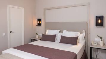 Un dormitorio ordenado con una cama grande, mesitas de noche y una lámpara fijada a la pared.