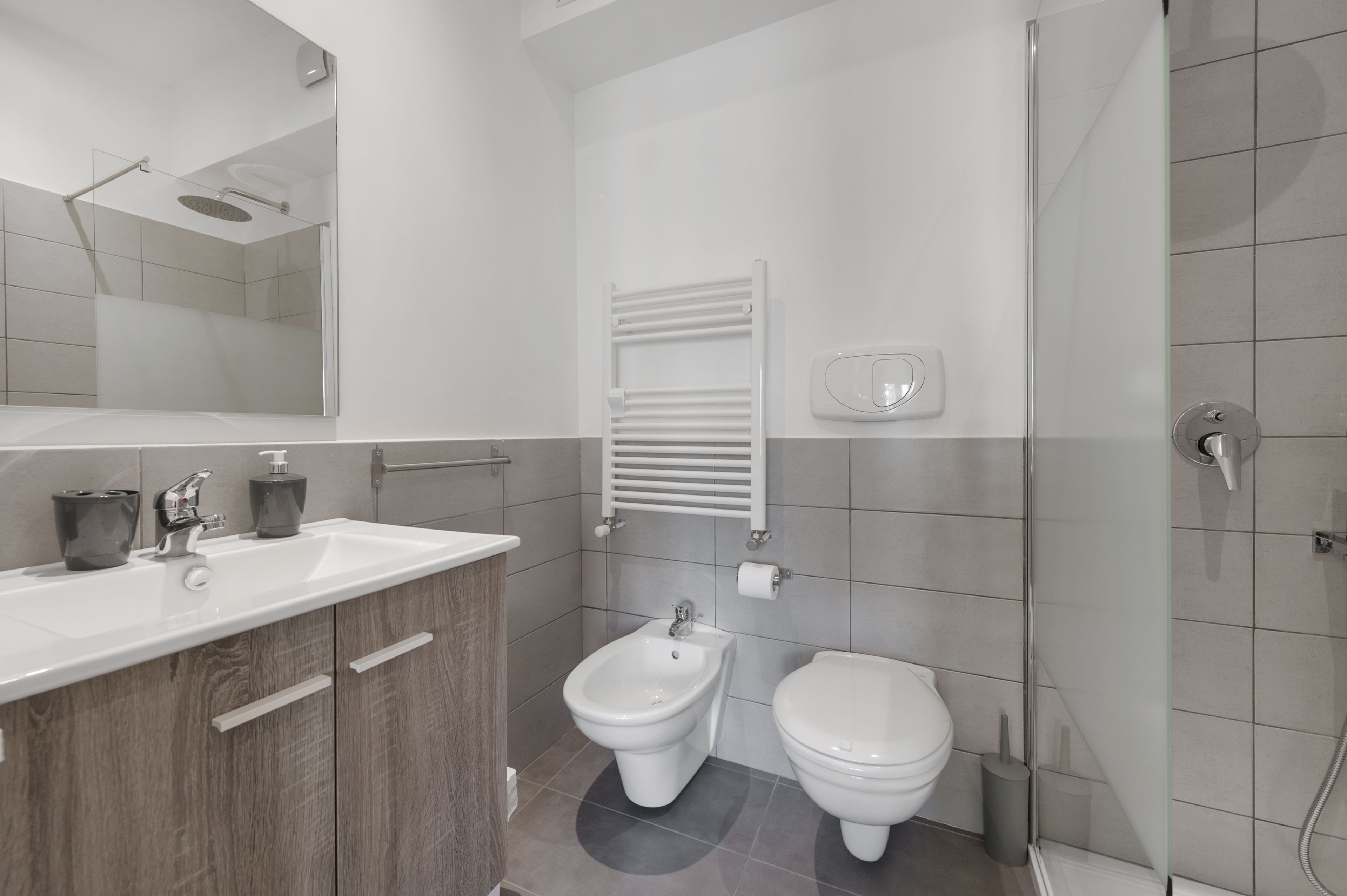 Un baño moderno con ducha, bidé, inodoro y tocador con espejo y lavamanos.