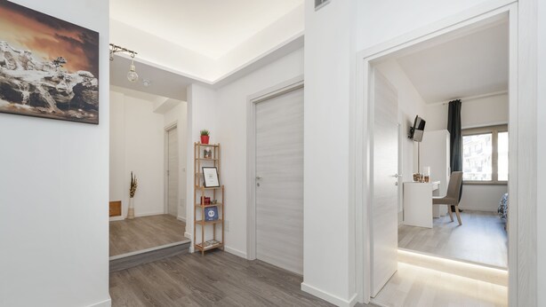 A modern interior with a wooden floor, a hallway leading to a bedroom, and a small seating area with a chair and a table. - De Guestibus (Rome)