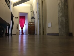 Un couloir avec un tonneau en bois, un rideau rouge et une lampe.