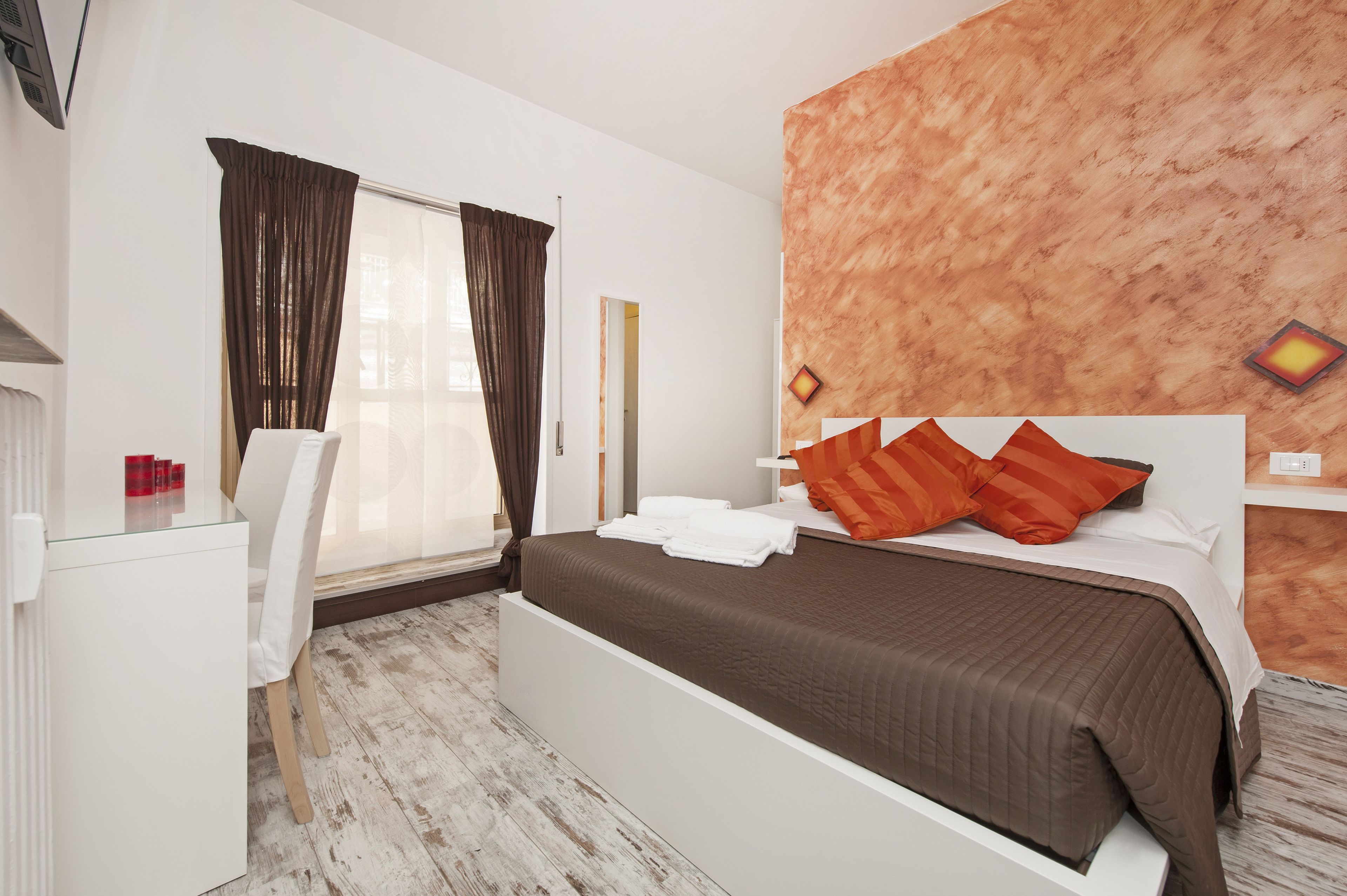 Quarto moderno com uma cama grande, uma escrivaninha branca e uma janela com cortinas.
