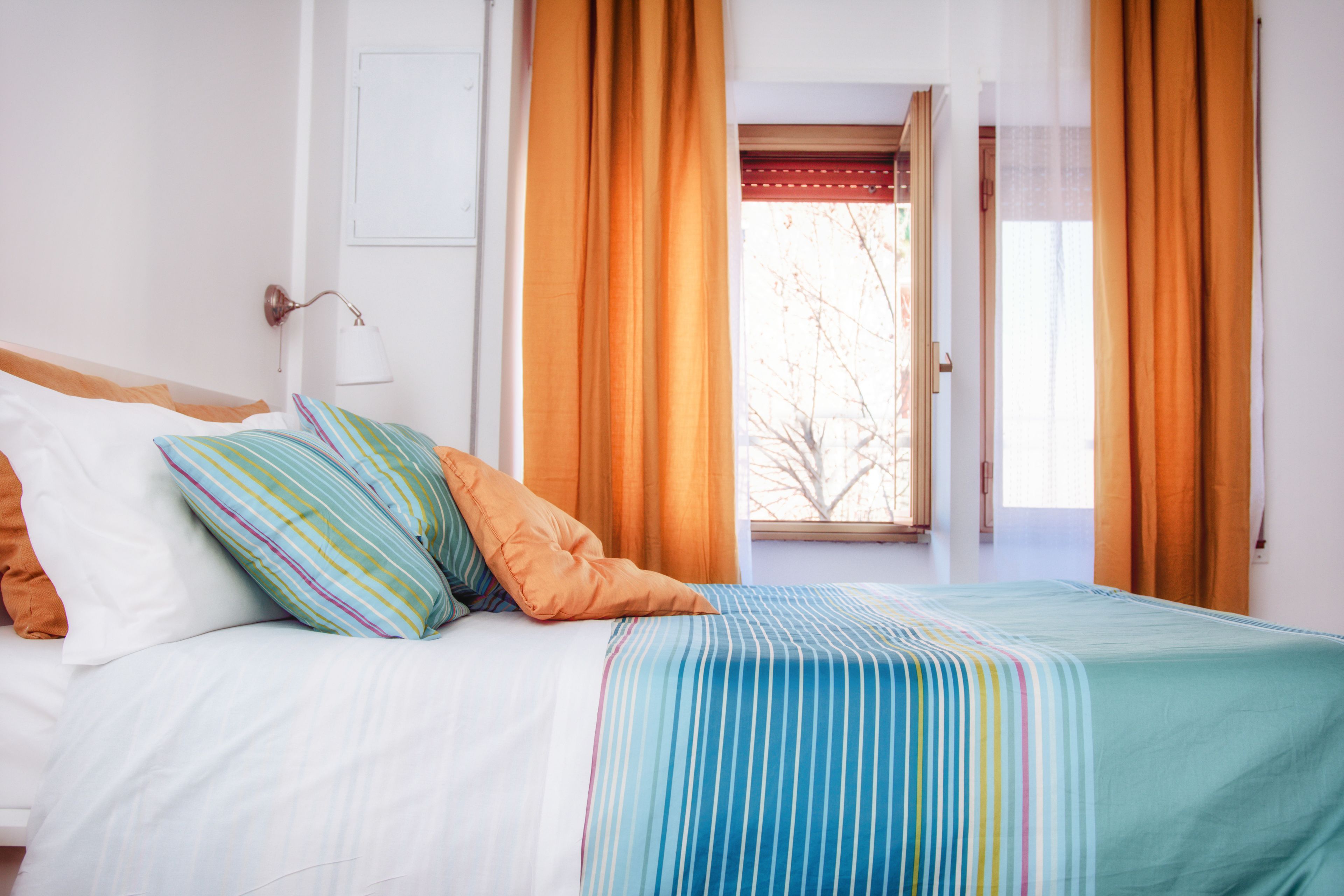 A bed with a striped bedspread, a white wall, and a window with curtains.