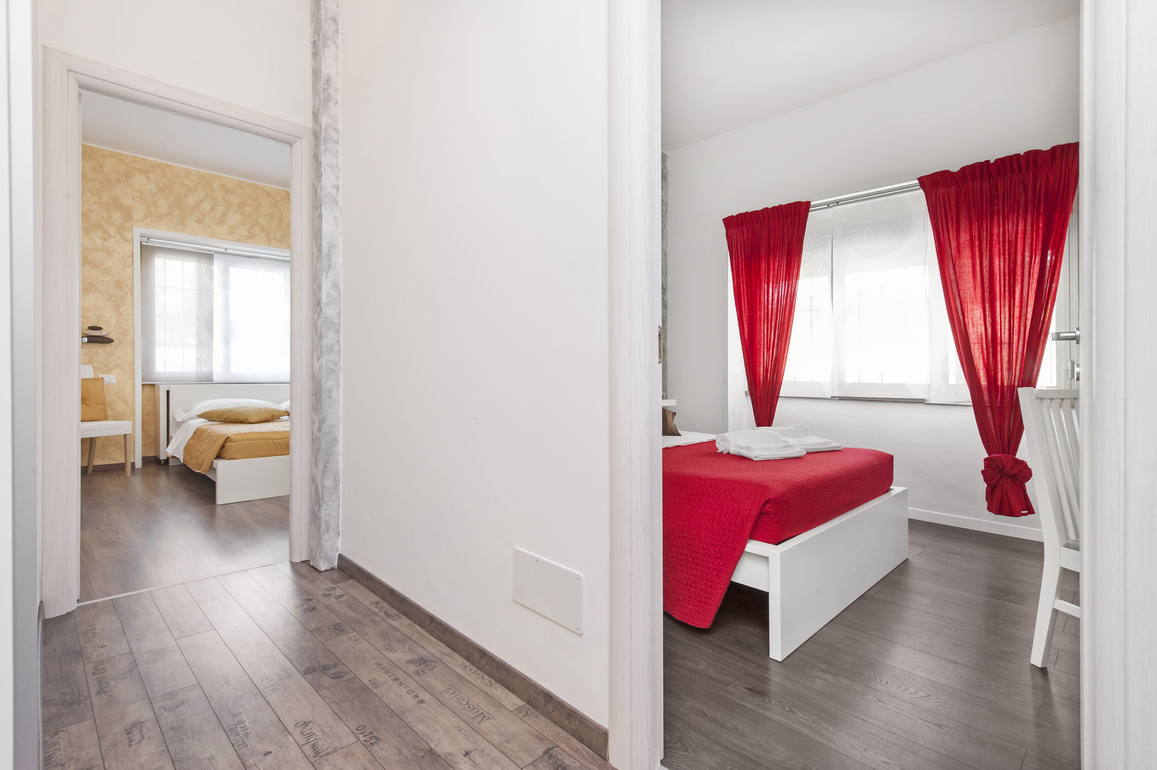 Een moderne slaapkamer met een wit bed, rode gordijnen en een houten vloer.