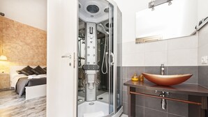 A modern bathroom with a glass-enclosed shower, a wooden vanity, and a large vessel sink. - De Guestibus (Rome)