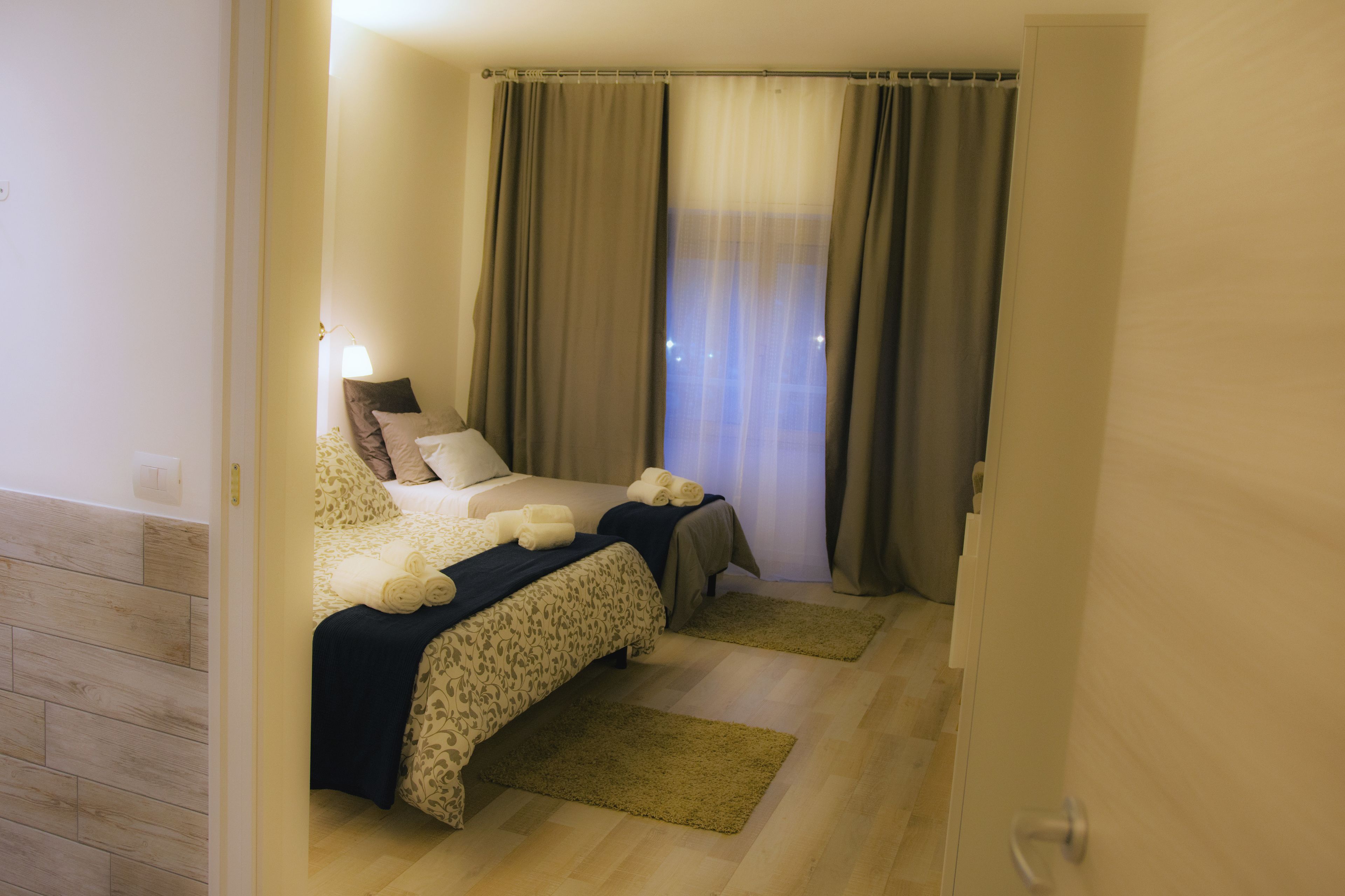 A bedroom with two beds, a wooden floor, and a window with curtains.