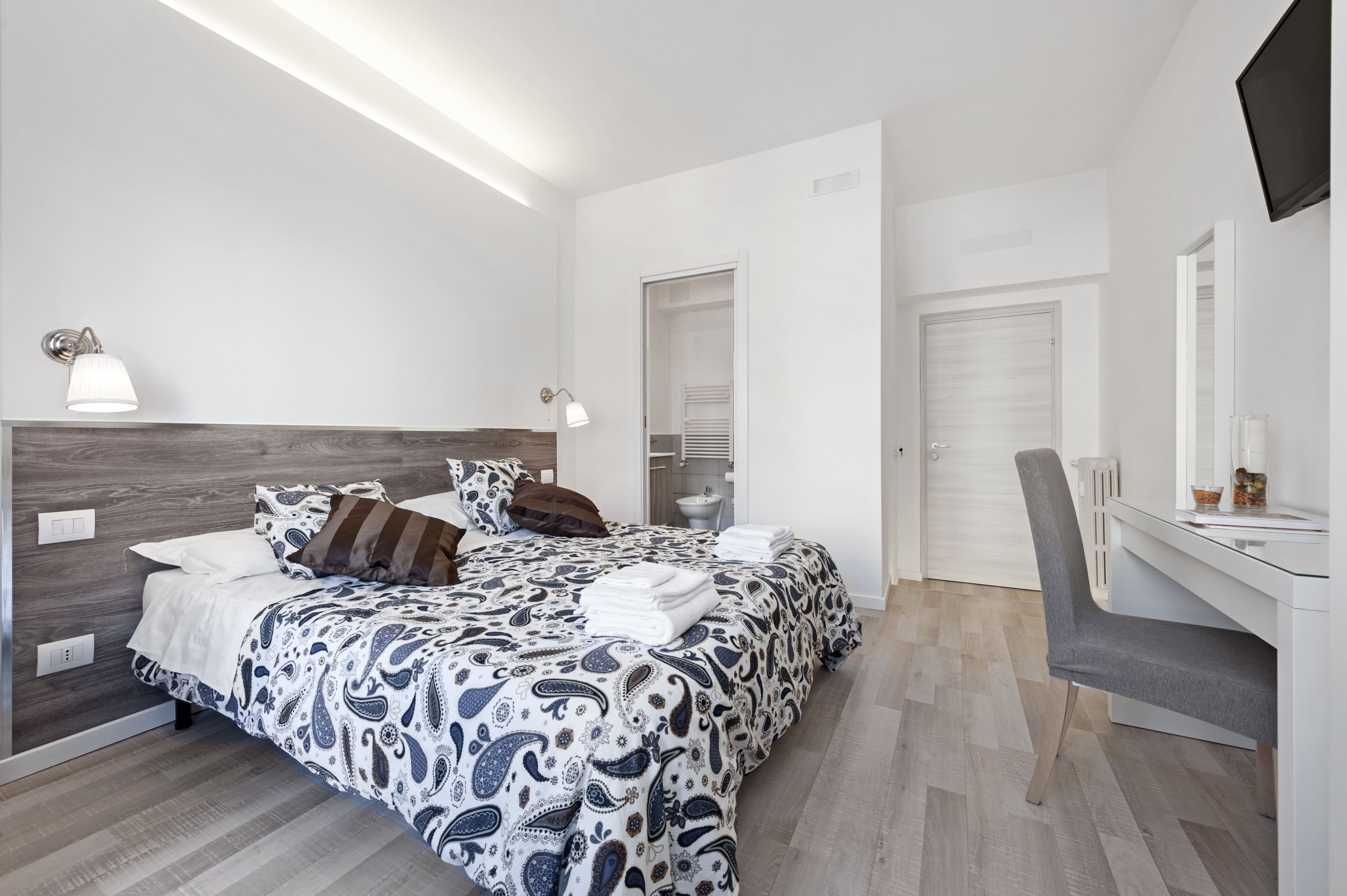 A modern bedroom with a large bed, bedside lamps, a desk, and a chair.