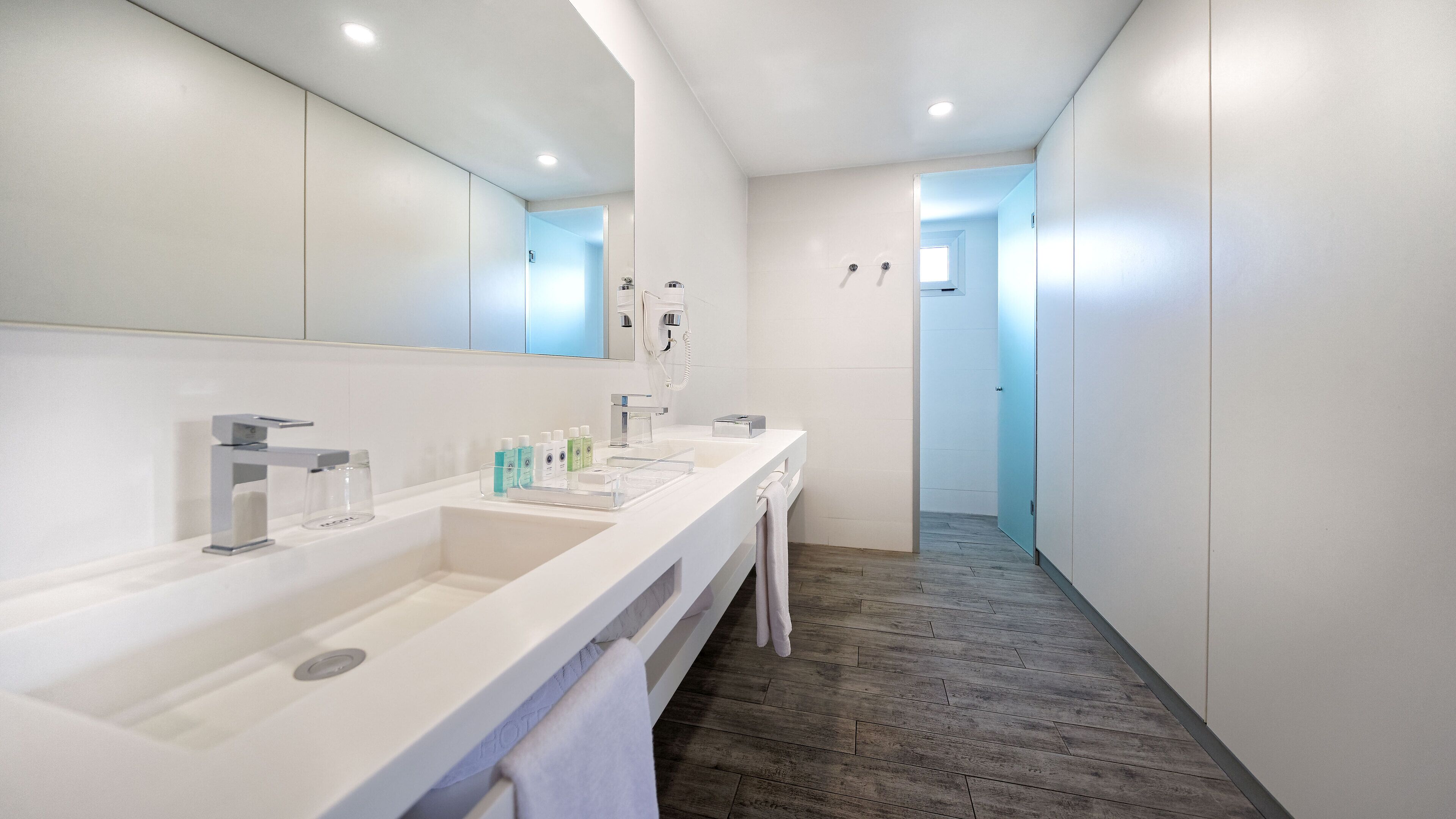 A modern bathroom with a long vanity, a large mirror, and a walk-in shower.