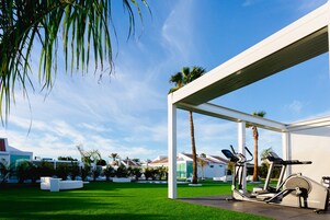 A modern outdoor gym area with exercise equipment, a covered seating area, and a well-maintained lawn.