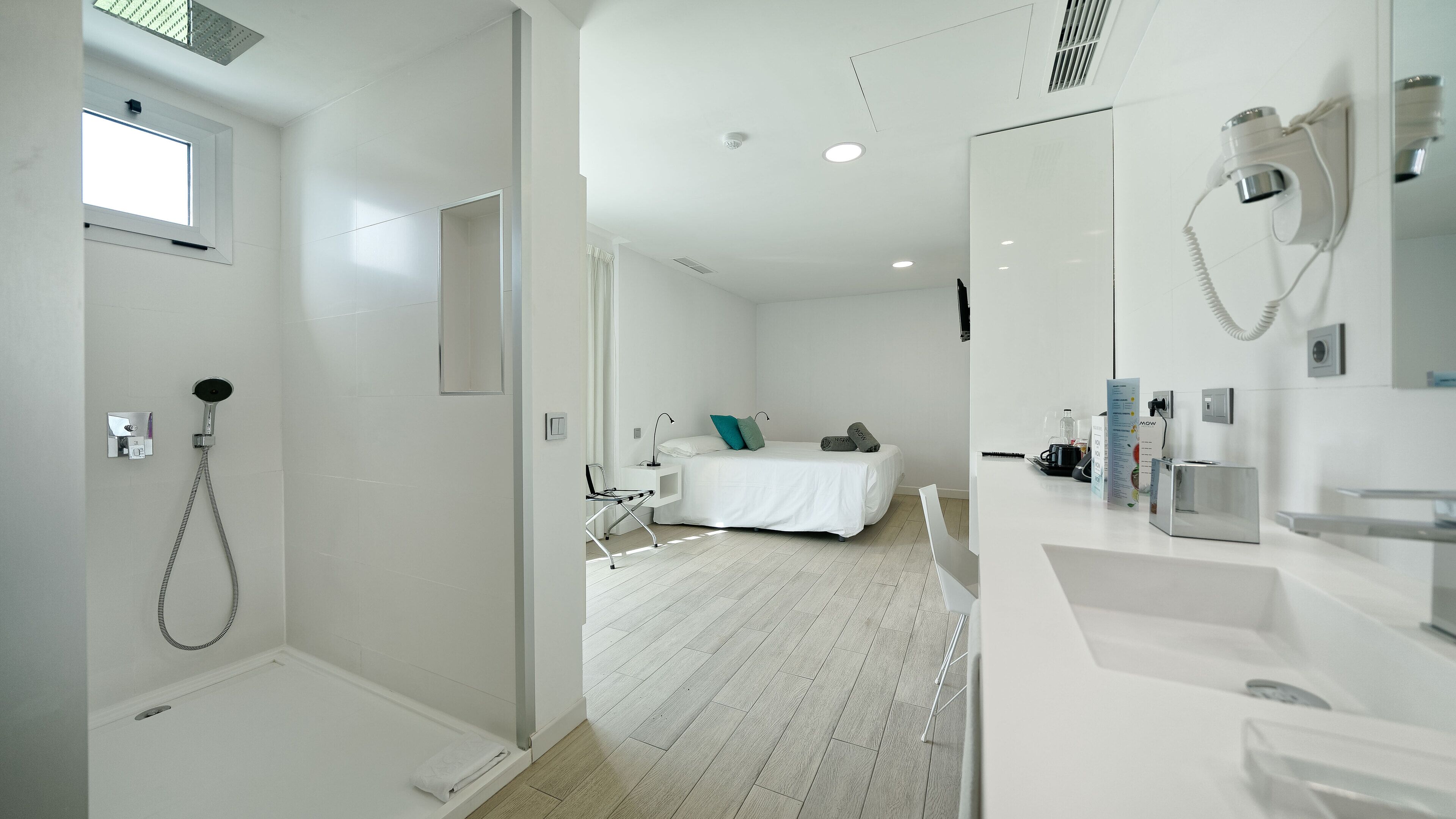 Una habitación de hotel moderna con ducha, cama, escritorio y baño con espejo y lavamanos.
