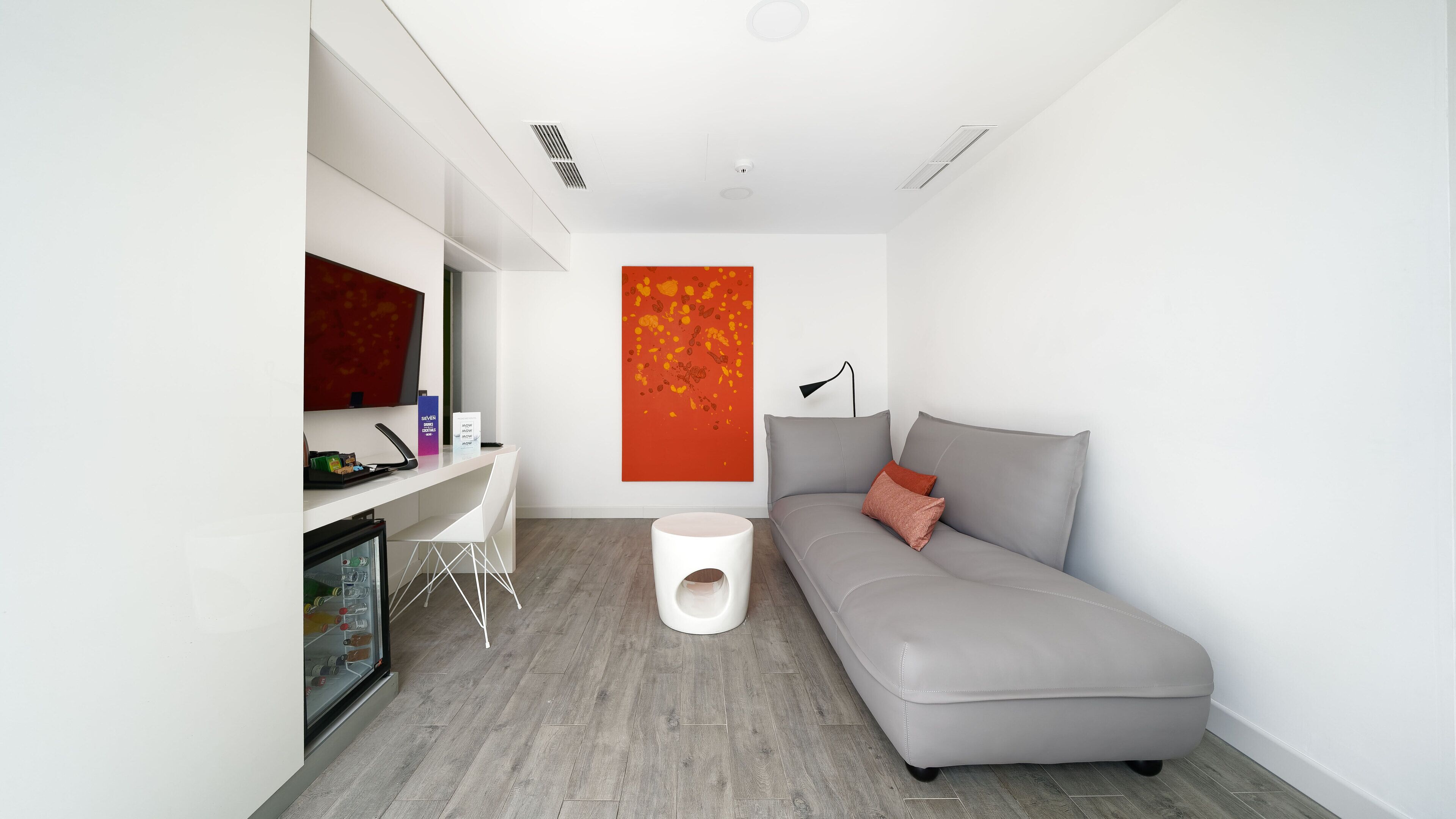 A modern, minimalistic room with a grey sofa, a white desk, and a large abstract painting on the wall.