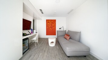 Quarto moderno e minimalista com um sofá cinzento, uma escrivaninha branca e um grande quadro abstrato na parede.