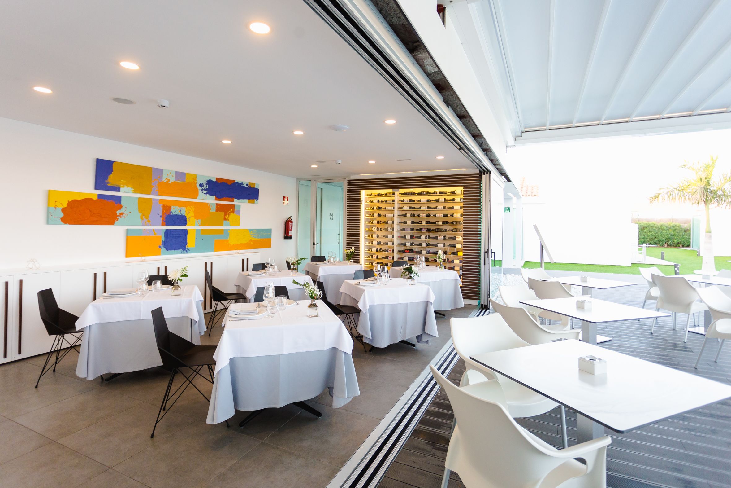 Un comedor moderno con mesas y sillas, una pared con arte abstracto y una estantería para vinos.