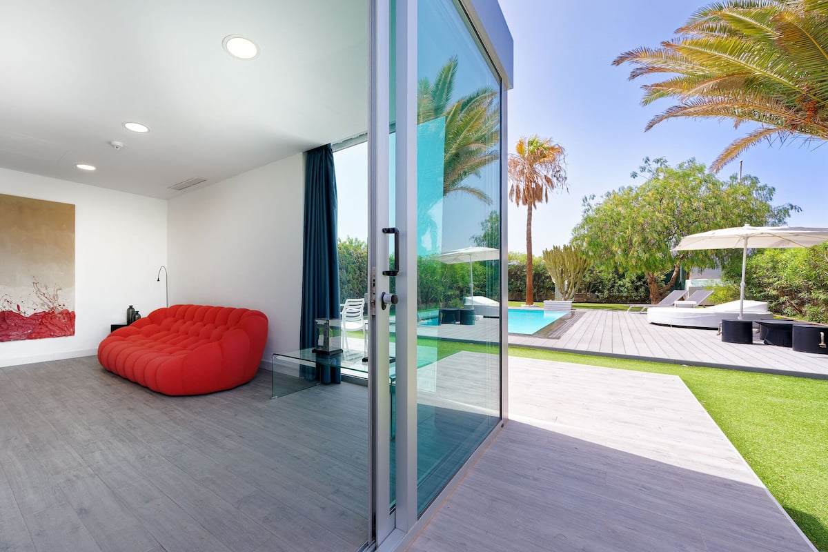Ein modernes Interieur mit einem roten Sitzsack, einer Glaswand und Blick auf einen Poolbereich im Freien.