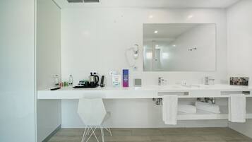 Un baño moderno con dos lavamanos, un espejo grande y una ducha. Hay artículos de aseo en el mostrador y un perchero con toallas.