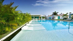 A swimming pool with clear blue water, surrounded by lush green palm trees and white lounge chairs. - Seven Hotel & Wellness - Caters to Gay Men (San Bartolomé de Tirajana)