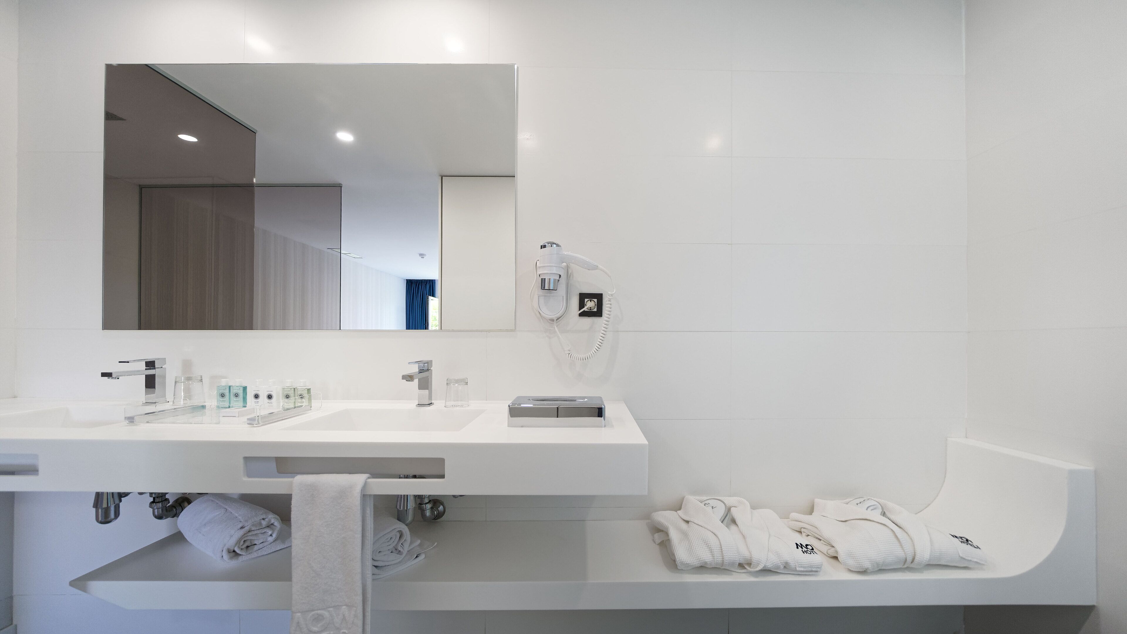 Een moderne badkamer met een grote spiegel, een haardroger en keurig opgevouwen handdoeken.