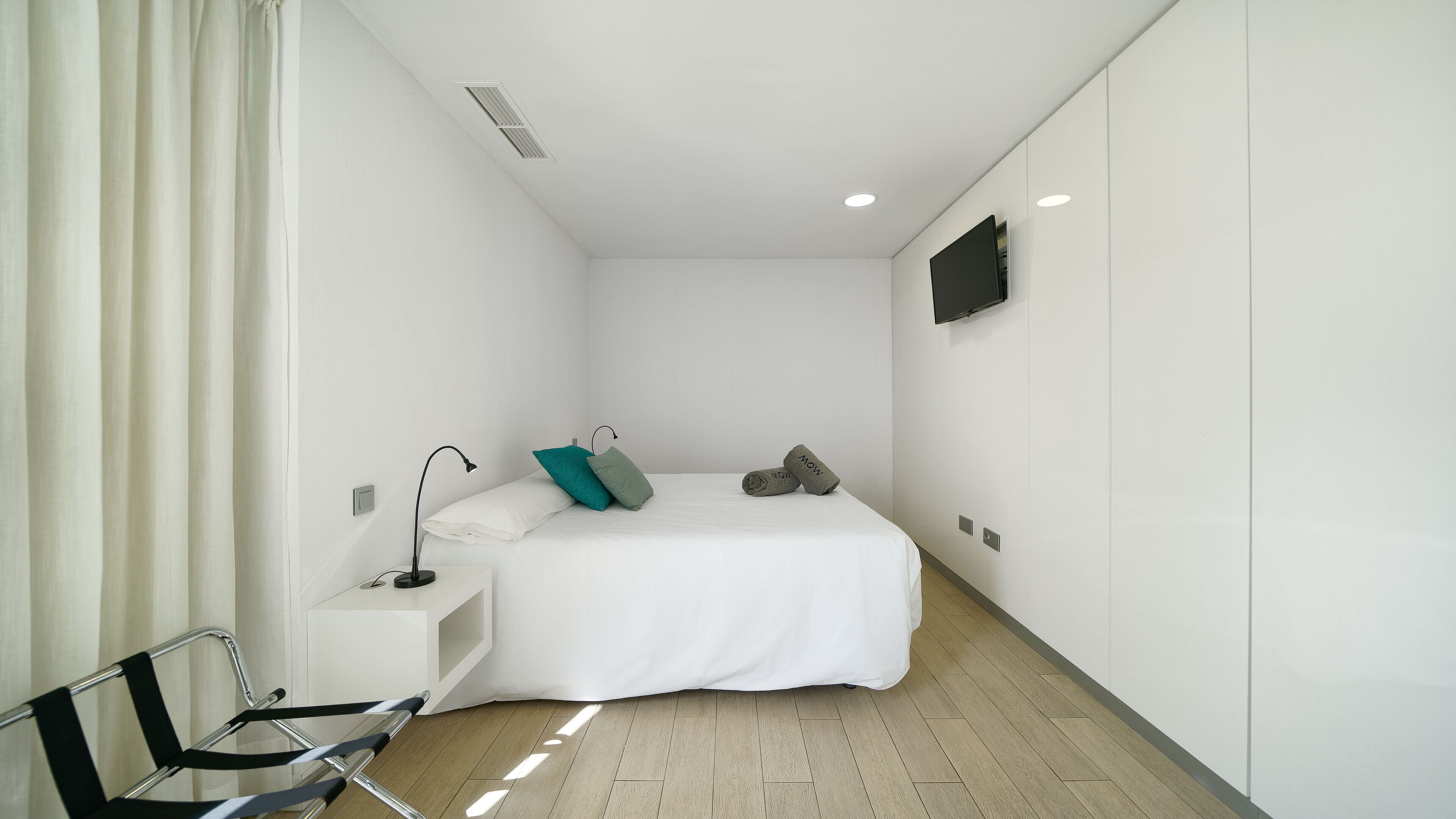 Un dormitori modern i minimalista amb un llit individual, una taula de nit, escriptori, cadira i televisió de pantalla plana penjada a la paret.